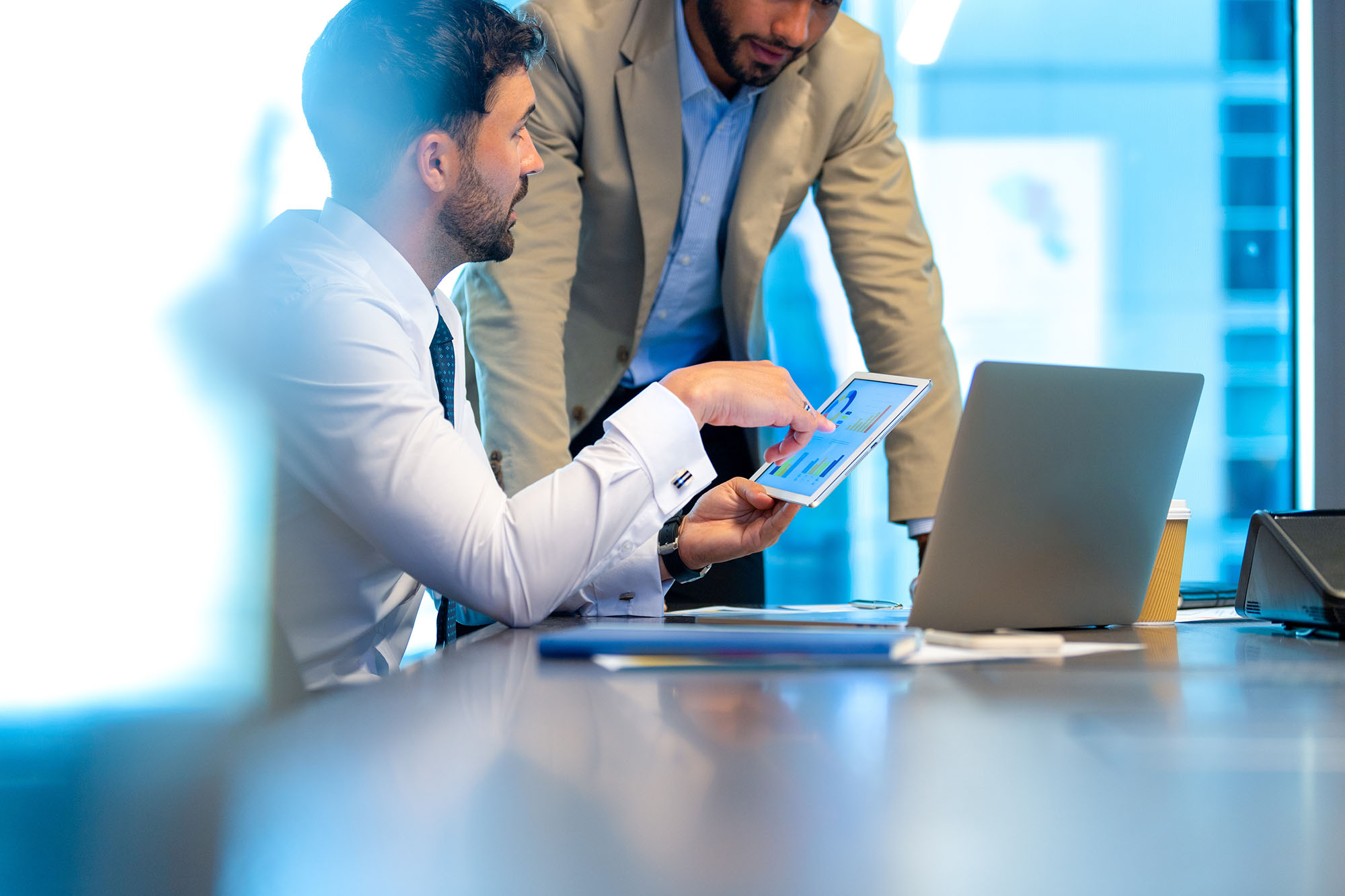 A business professional reviewing cybersecurity performance metrics on a tablet during a meeting, illustrating data-driven cyber resilience discussions within an investment firm.